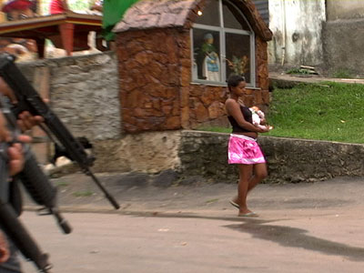 Eine Frau mit einem Kind geht unbeeindruckt an einer Polizei-Streife in Morro dos Macacos vorbei.