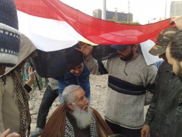 De vader van Nadia en andere demonstranten schuilen voor de regen onder de Egyptische vlag