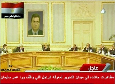 Reunión simulada del gabinete egipcio realizada ante una foto del 'hombre detrás de Omar Suleiman'. La leyenda de la noticia abajo dice "Enorme manifestación realizada en Plaza Tahrir para descubir la identidad del hombre detrás de Omar Suleiman". Imagen de la cuenta de TwitPic de BehindOmarSuleiman.