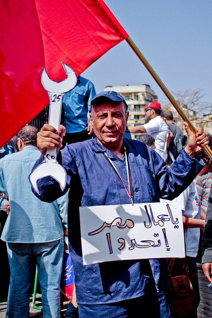 One of the protesters in Tahrir Square during the Labour Day celebrations, carrying one of the most famous quotes taken from The Communist Manifesto by Karl Marx and Friedrich Engels, Workers of The World, Unite! Photo by Maggie Osama used under Creative Commons (CC BY-NC-SA 2.0).