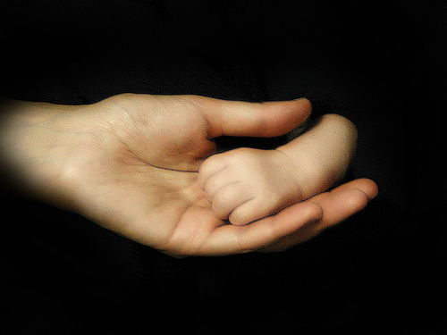 mother holding infant son's hand on a black background
