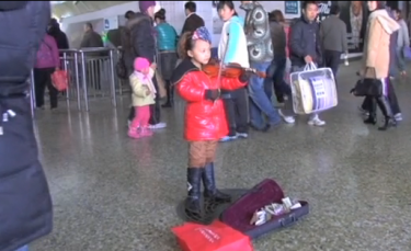 Devojčica svira violinu za napojnicu na železničkoj stanici u Pekingu. Kadar iz trejlera dokumentarca snimljen u novembru 2010.