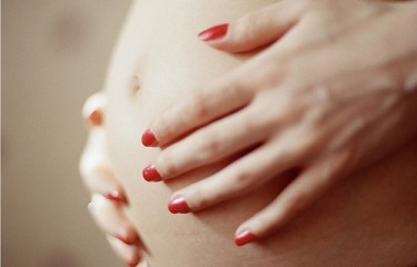 woman with red fingernailed hands over pregnant belly
