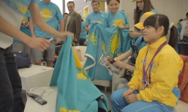 Zulfia Chinshanlo surrounded by fans of the Kazakhstan team after claiming a gold medal in weightlifting. Screenshot from video "Chinshanlo delights in Olympic gold' uploaded July 30, 2012, by YouTube user SNTVonline.