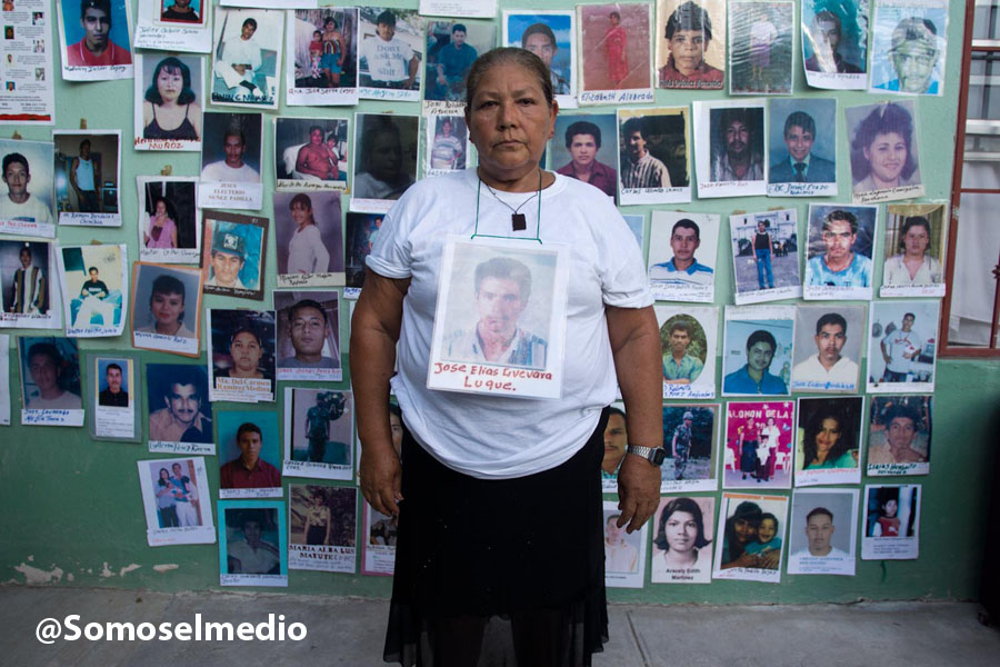 Mother participating in the caravan stands in front of photos of missing migrants.