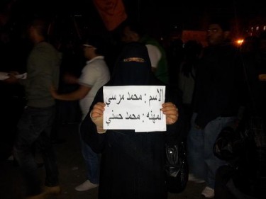 Eine Demonstrantin hält ein Schild, auf dem steht [ar]: Name: Mohammed Mursi; Beruf: Mohammed Hosni