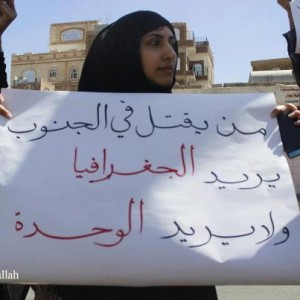 A protester holding a placard that reads in Arabic "He who is killing in the south wants the geography and does not want the unity"