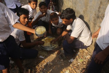 Studenti di una scuola di Mumbai mangiano seduti per terra senza sedie nè piatti