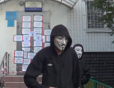 Two Navalny's Brothers activists in "Anonymous" masks leave after pasting campaign materials on the door of a Moscow police department. YouTube screenshot.