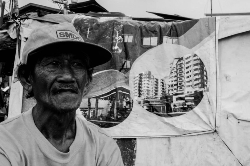 رجل يرتدي قبعة إس إم. إس إم مملوكة لرجال الأعمال الفلبينيين الأغنياء. يوجد خلفه قماش معروض عليه بعض مشاريع البناء.