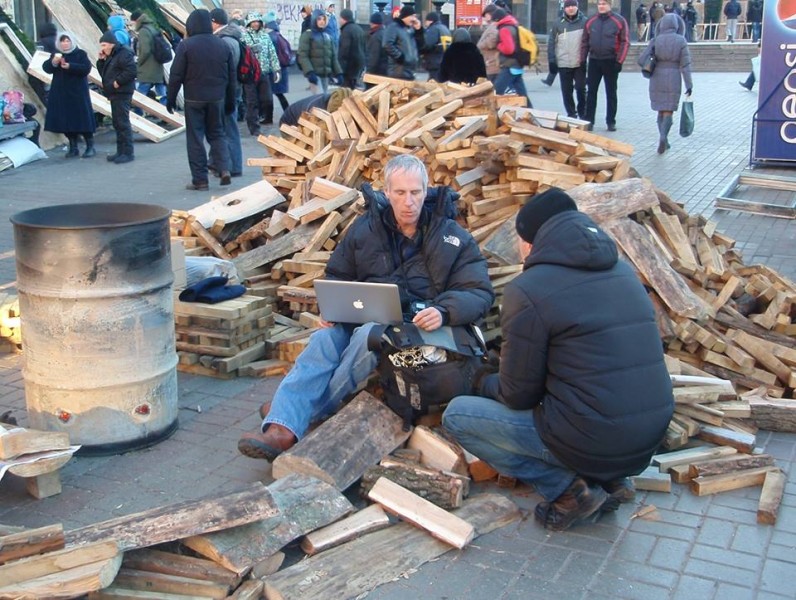 A man holds his laptop while sitting on chopped wood amid protesters in Kyiv, Ukraine. Photo by Dima Kravchuk. Used with permission.