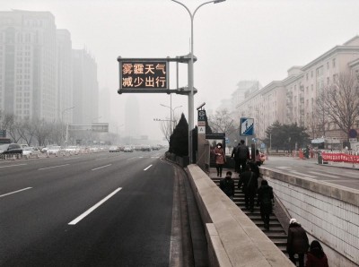 Foto autora. Těžký smog pohlcující Peking ke konci února 2014. Elektronická dopravní deska oznamuje :"Omezte venkovní aktivitu během smogové situace." 