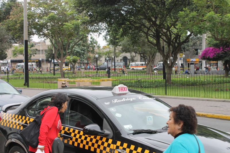 A passenger interacts with the driver of a Lima taxi sporting the new regulation black-and-yellow stripes and lighted sign. Some Lima residents say marking licensed taxis in this way will make them feel safer. Photo by Alex Pashley.