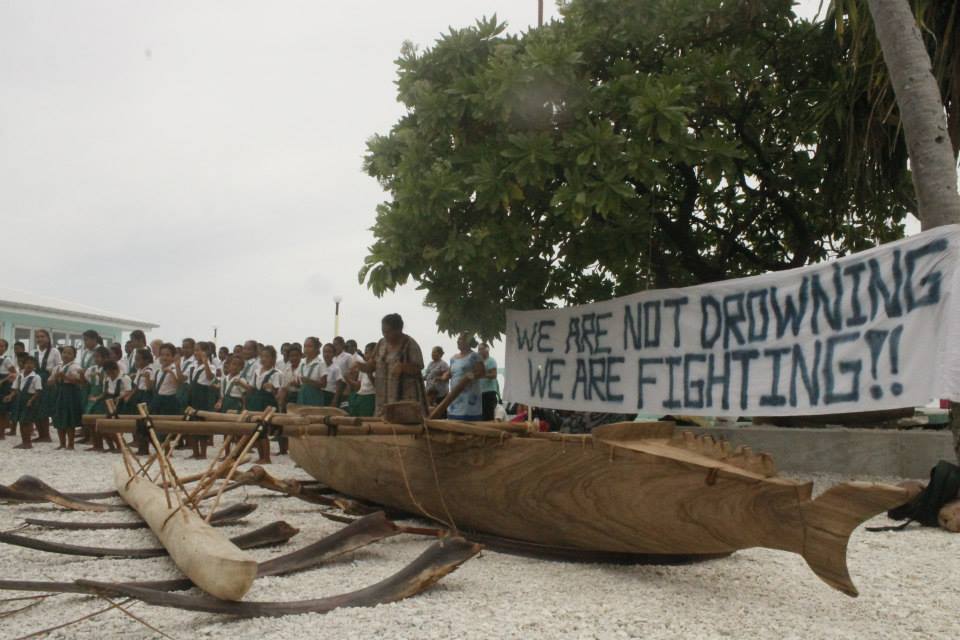 Tokelau school-kids with canoe and banner which reads: "We Are Not Drowning We Are Fighting." Photo credit: 350.org