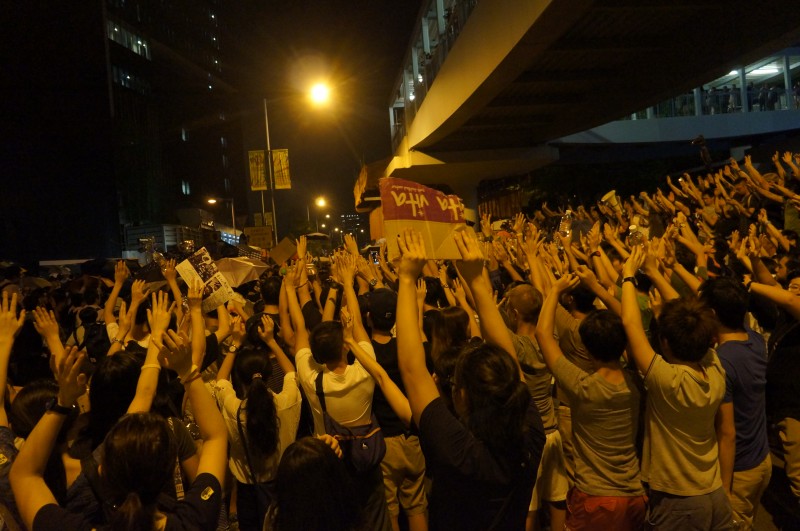 Protestujący utworzyli tarczę ludzką i podnieśli ręce pokazując, że są nastawieni pokojowo. Jednak policja nie zaprzestała użycia gazu pieprzowego. Zdjęcie z inmediahk.net. 