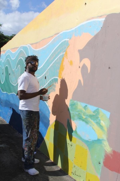 Haitian artist, Prensnelo, paints the armadillo of the Grenada climate change mural. Photo courtesy the artists; used with permission. 