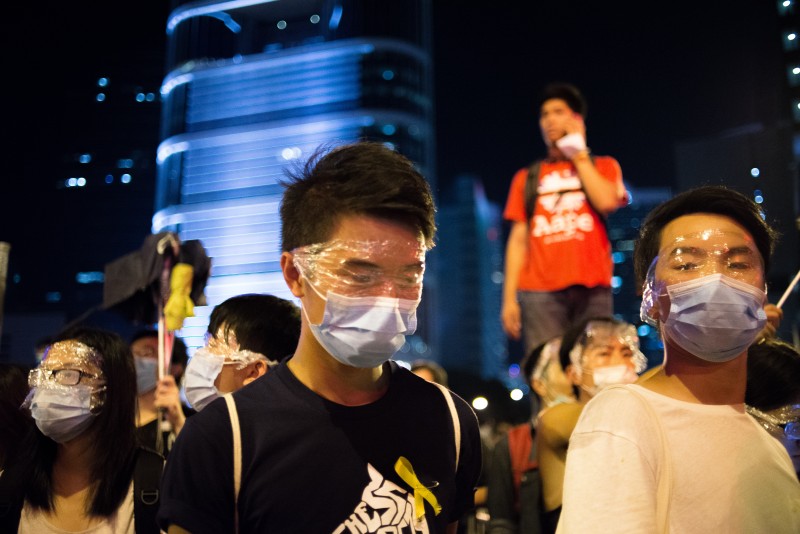 Protestující u úřadu vlády v Hongkongu používají celofánové fólie a chirurgické roušky, aby se chránili proti pepřovému spreji. Autor fotografie Robert Godden, 27. září 2014. Copyright Demotix.