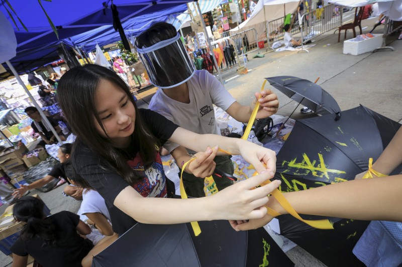 Protestující váží žluté stužky na ruce zájemců během hongkongského protestu v oblasti Causeway Bay. Autor fotografie Guillaume PAYEN, 1. října 2014. Copyright Demotix.