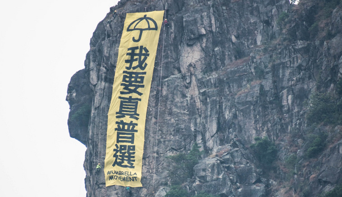 A group of mountain climbers hang a huge banner, "I want genuine universal suffrage" in Lion Rock, one of the most well-known landscape in Hong Kong.  The group explained their action to local media: “We were shock[ed] by CY Leung’s viewpoint that the poor should not have equality in election[s] and hope this action would be able to call public attention on the importance of universal suffrage.” Image from Hong Wrong.