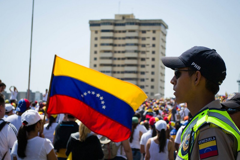 Policejní příslušník dohlíží nad protesty ve venezuelském městě Maracaibo, rok 2014. Autorka fotografie María Alejandra Mora, zdroj Wikimedia (CC BY-SA 3.0).
