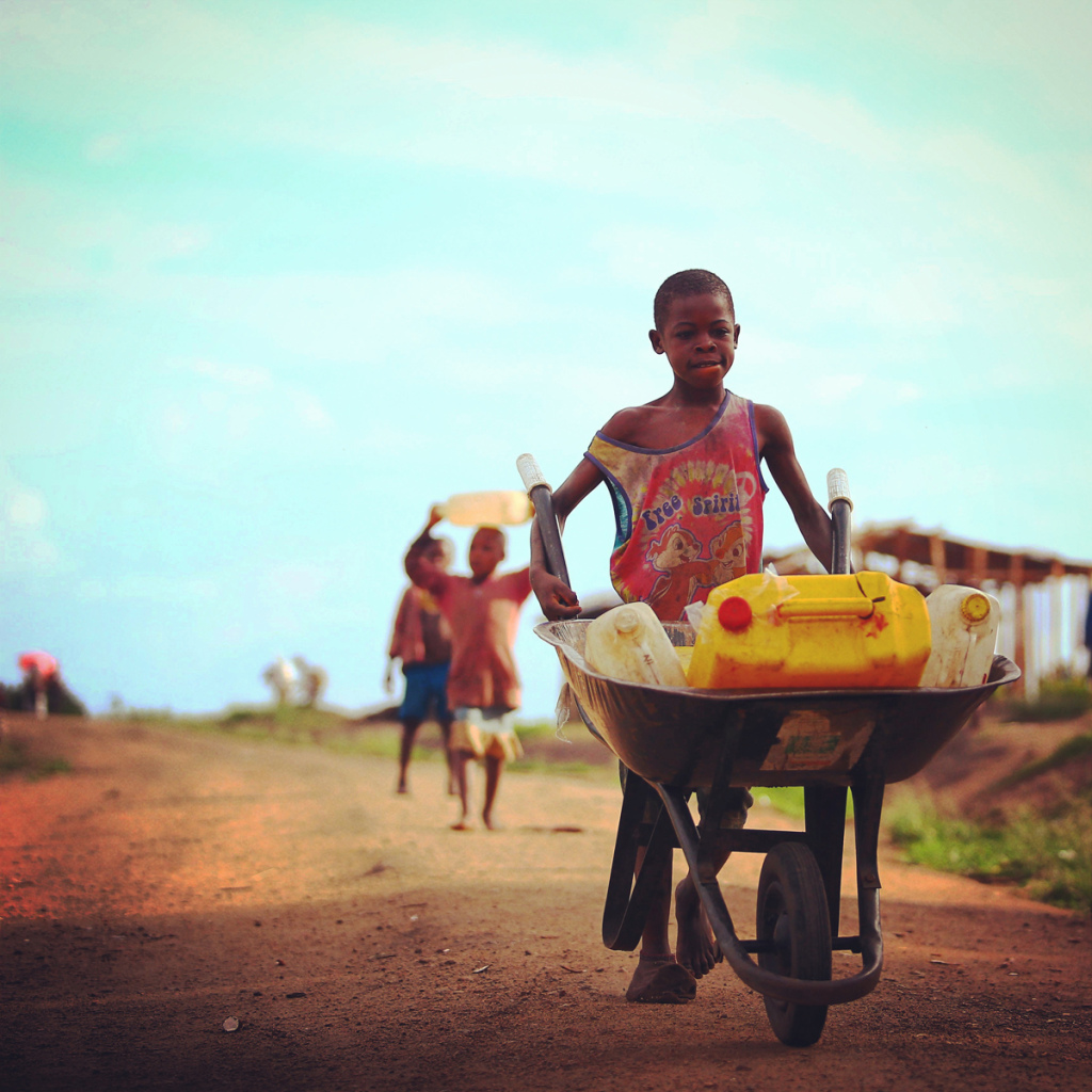 Une des photos de Edward Echwalus montrant un garçon pousser une brouette chargée de bidons remplis d'eau en Ouganda occidental. Photo utilisée avec la permission.