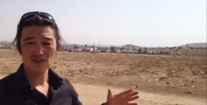 Kenji Goto raportanta ekster la urbo Kobani, Sirio, en 2014. Ekrankopio el la ĉefpaĝo de SnapcastNews en Jutubo.