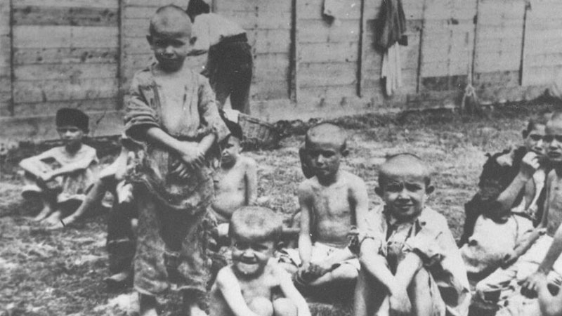 Děti sedí před jednou z ubytoven v koncentračním táboře Sisak. Volně šiřitelná fotografie.