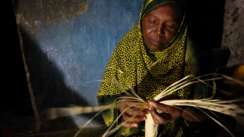 Kanoa Sharif Haji, a 45 year old mother of eight, weaves reed mats at night under a bright solar powered LED light at her home in Matemwe. This new work at night earns her family an extra fifteen dollars a month, a huge amount in these parts. Credit: Sam Eaton. Published with PRI's permission