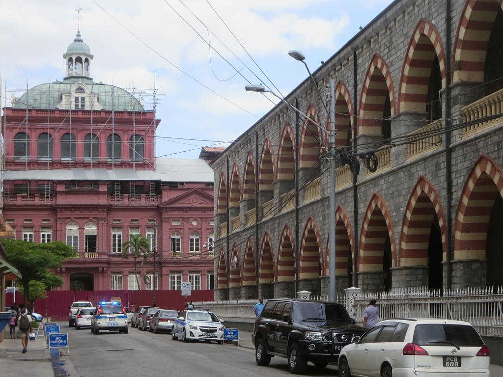 The neo-Gothic Old Police Headquarters on Sackville Street in Port of Spain, Trinidad, frames the country's parliament building, Renaissance-style Red House (1906), which was stormed by insurgents of the Jamaat-al-Muslimeen on July 27, 1990.  Photo by David Stanley (CC BY 2.0).