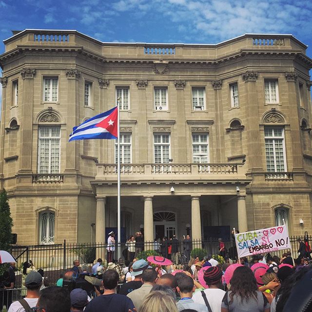 Вашингтон, США.  20 июля 2015 года - Народ наблюдает поднятие кубинского флага у посольства Кубы в Америке. Изображение взято со страницы пользователя Justin Feltman соцю сети  Instagram   -- Люди собрались у здания посольства, открывшегося заново спустя 54 года после закрытия, чтобы увидеть поднятие флага Кубы. В этот день народ отмечал полное восстановление дипломатических отношений между странами.