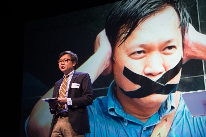 File photo of Thai journalist Pravit Rojanaphruk speaking in the 2015 Oslo Freedom Forum. He is also featured in the background photo of an anti-Junta protest demanding the protection of free speech in Thailand. Photo by Julia Reinhart, copyright @Demotix (5/26/2015)